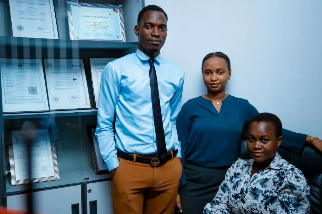 Three Zatra Consultants staff beside the firm's framed registration and completion certificates.